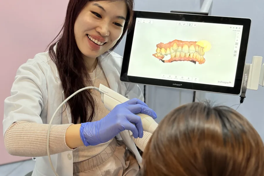 A dentist at FTS Chin Dental using a digital intraoral scanner, with the 3D scan of the teeth shown on the monitor beside her